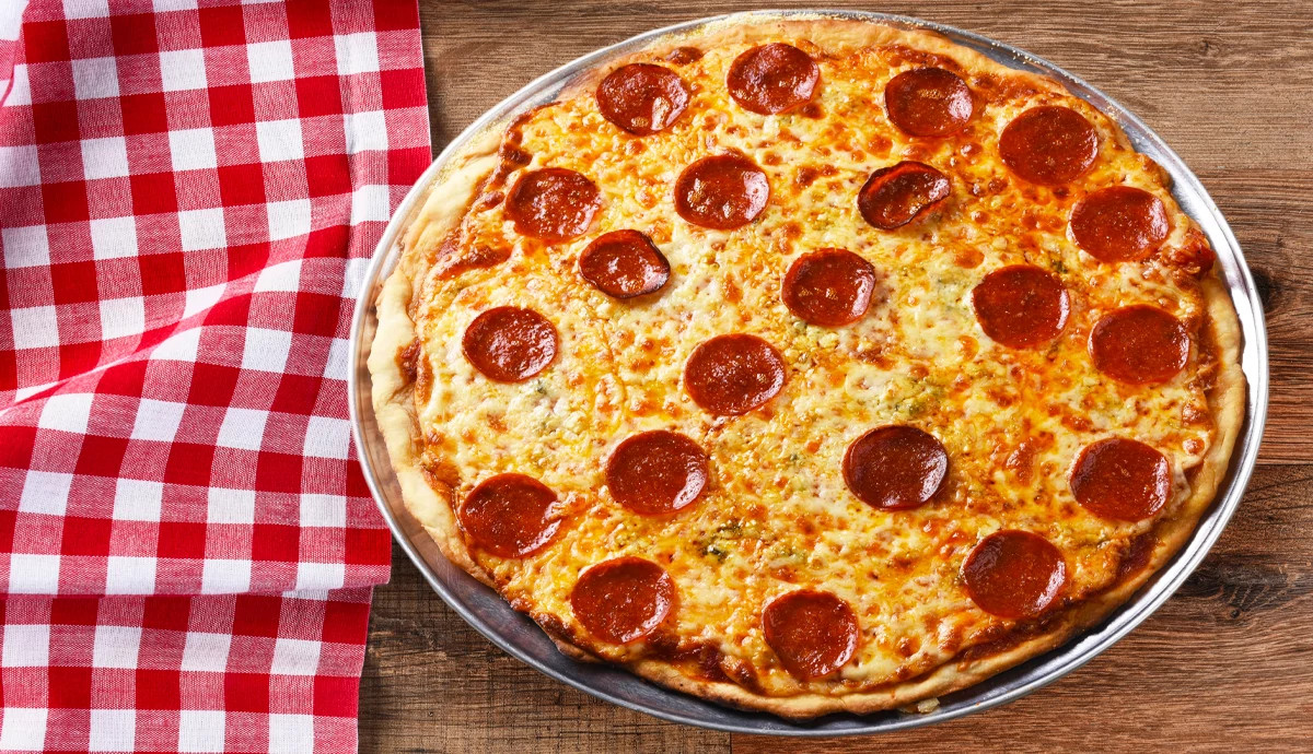 a pepperoni pizza is shown on a wood table next to a red checkered table cloth 