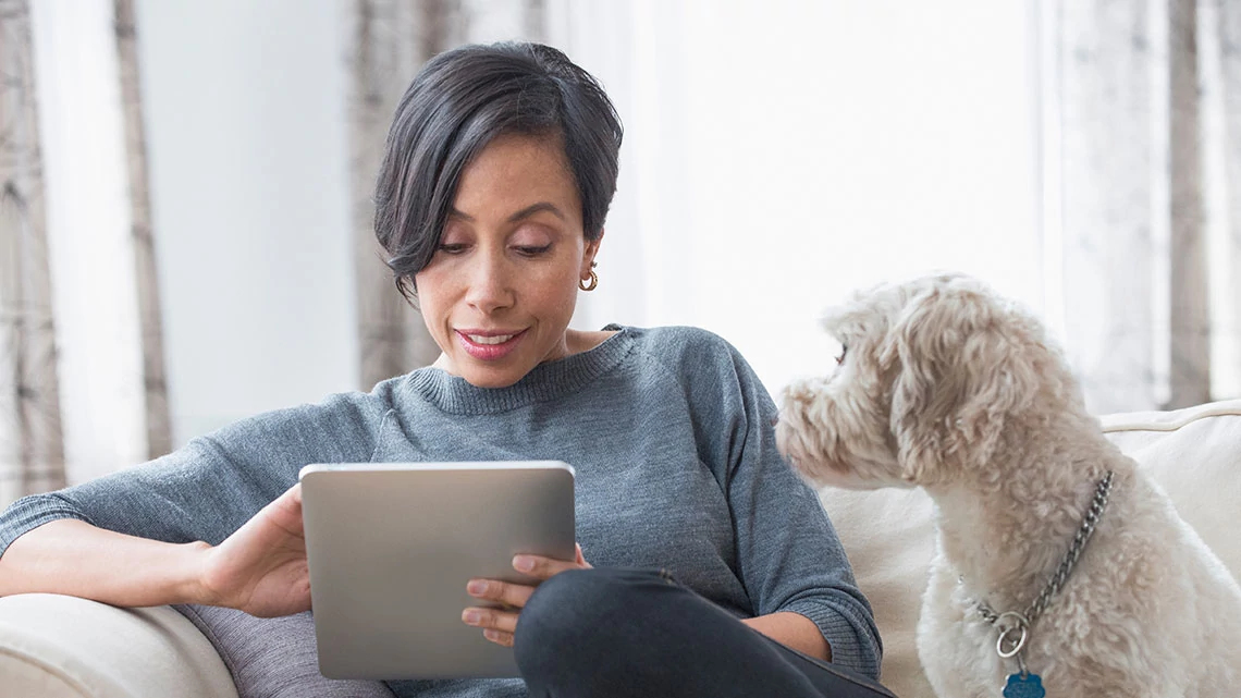 lady and dog with tablet in hand sitting on couch touching screen