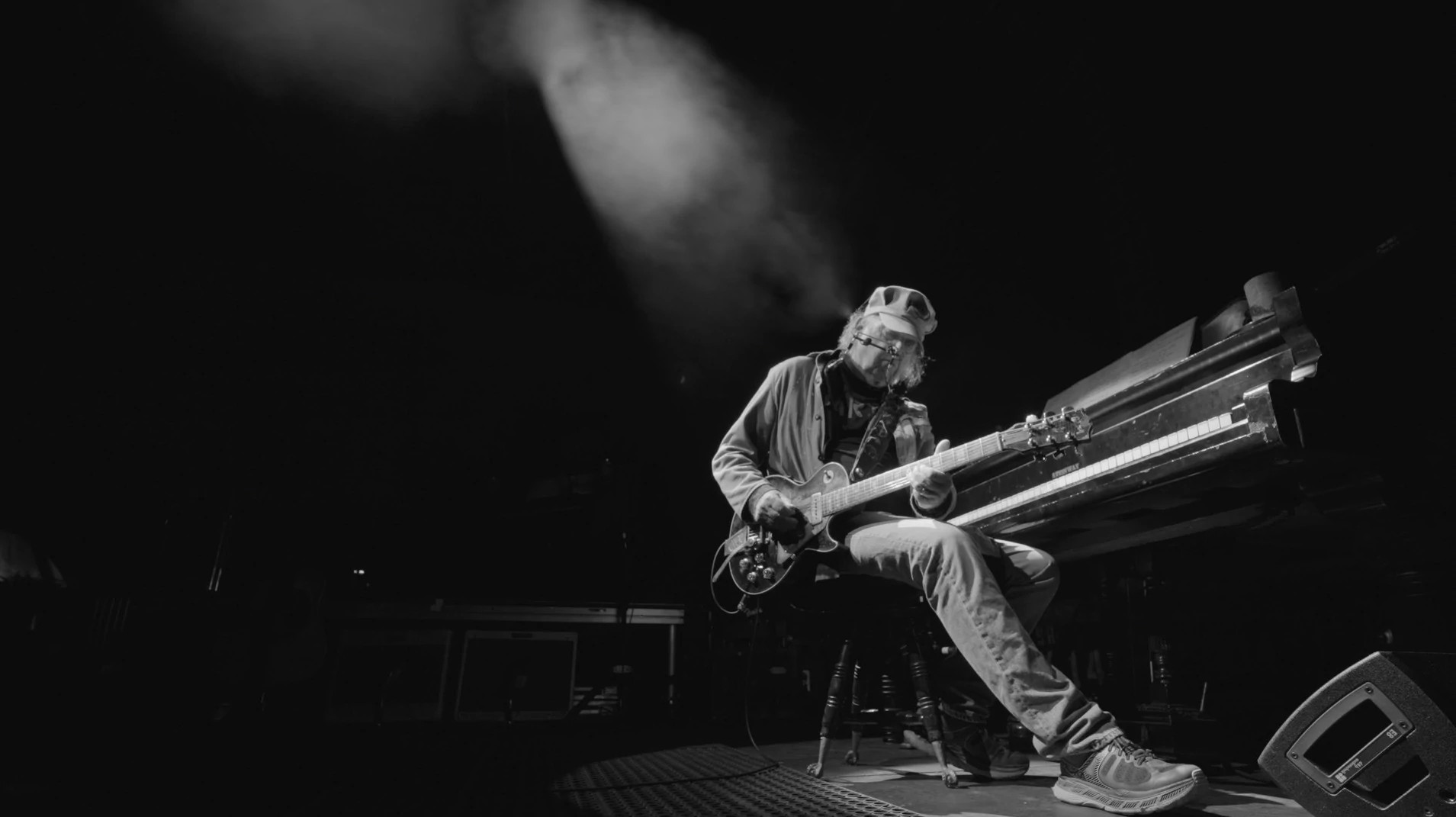 neil young playing a guitar onstage while seated on a stool