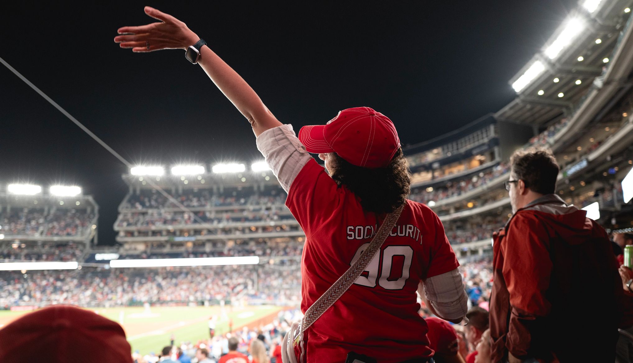 AARP Honors Social Security a person wearing a red baseball jersey raises their hand at a stadium