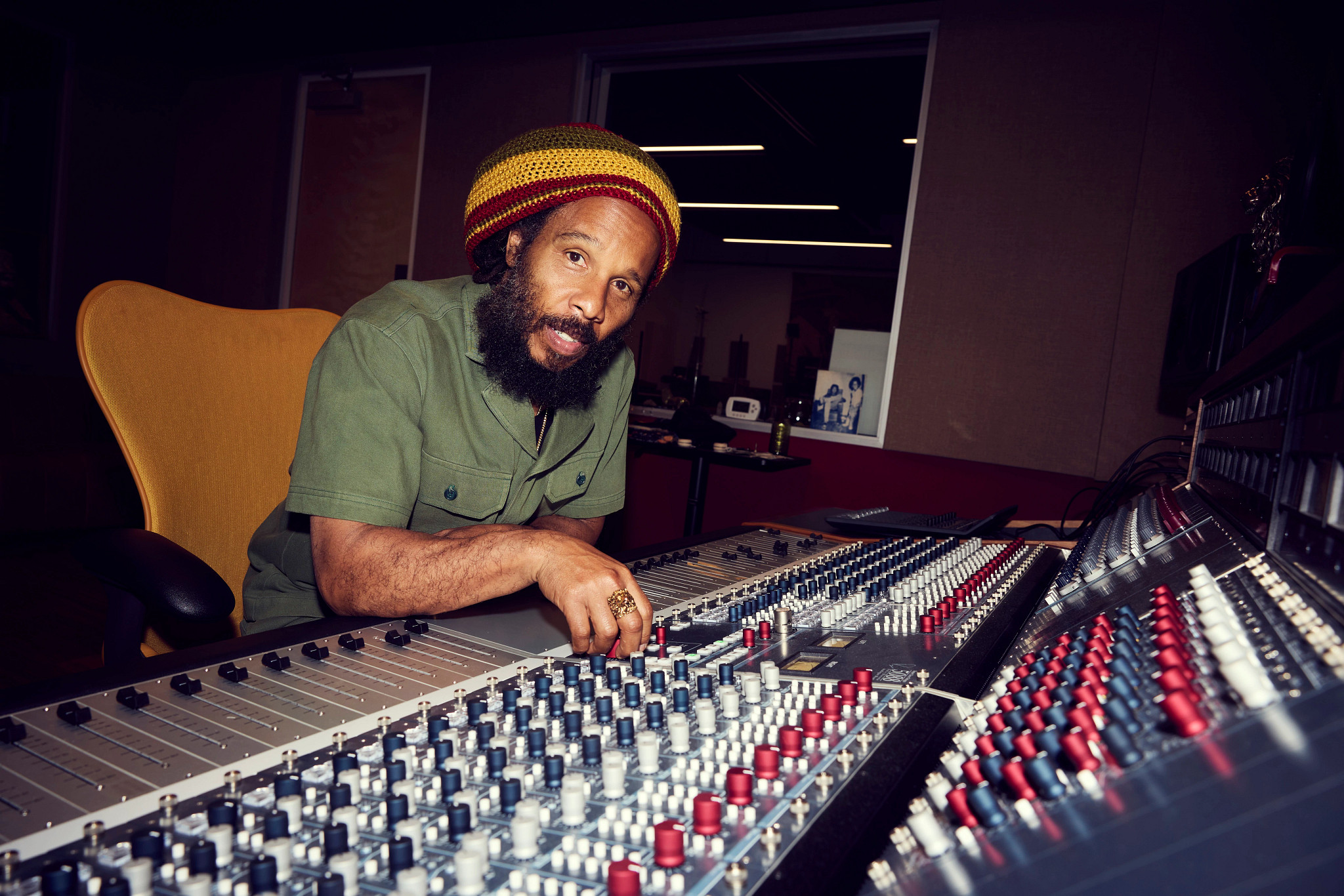 ziggy marley seated in front of an audio production control board in a recording studio