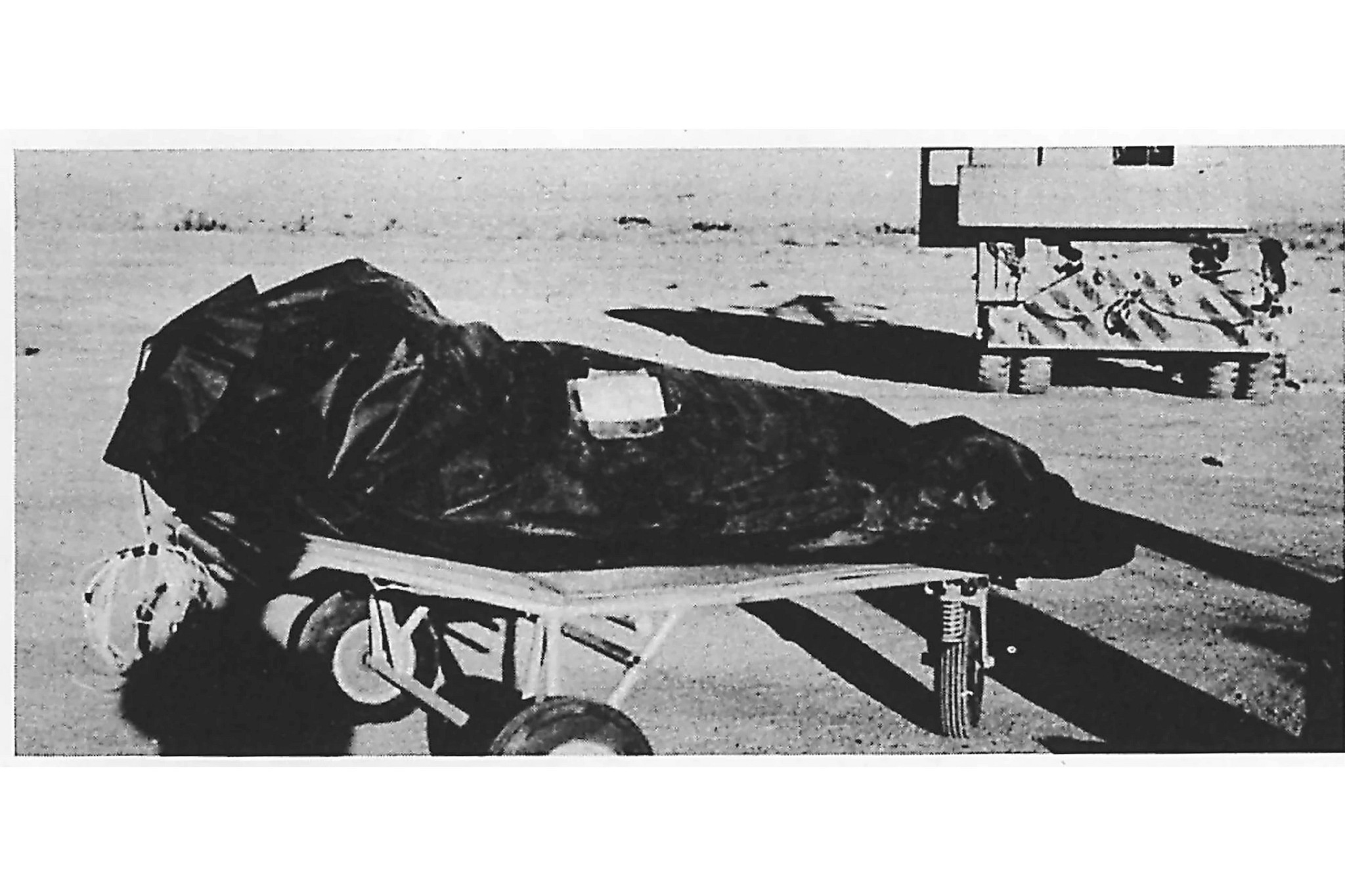 black and white photo shows a body bag on a gurney