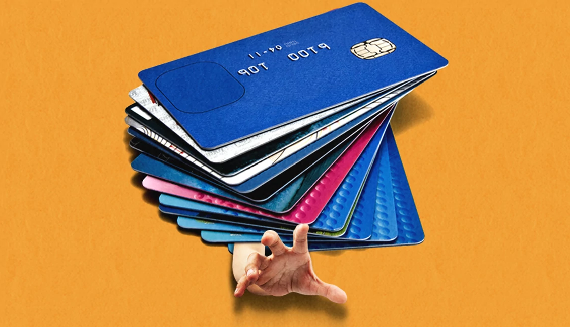una serie de tarjetas de crédito con una mano intentando salir de debajo