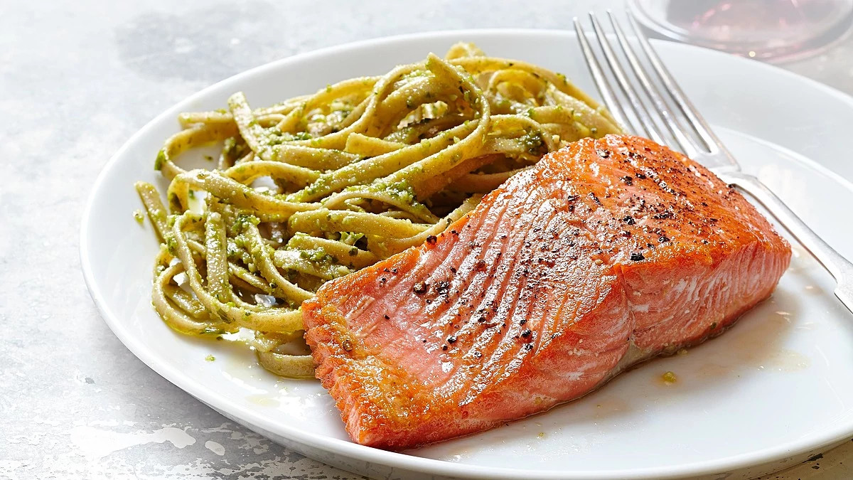 A close-up view of seared salmon with pesto fettucine on a plate