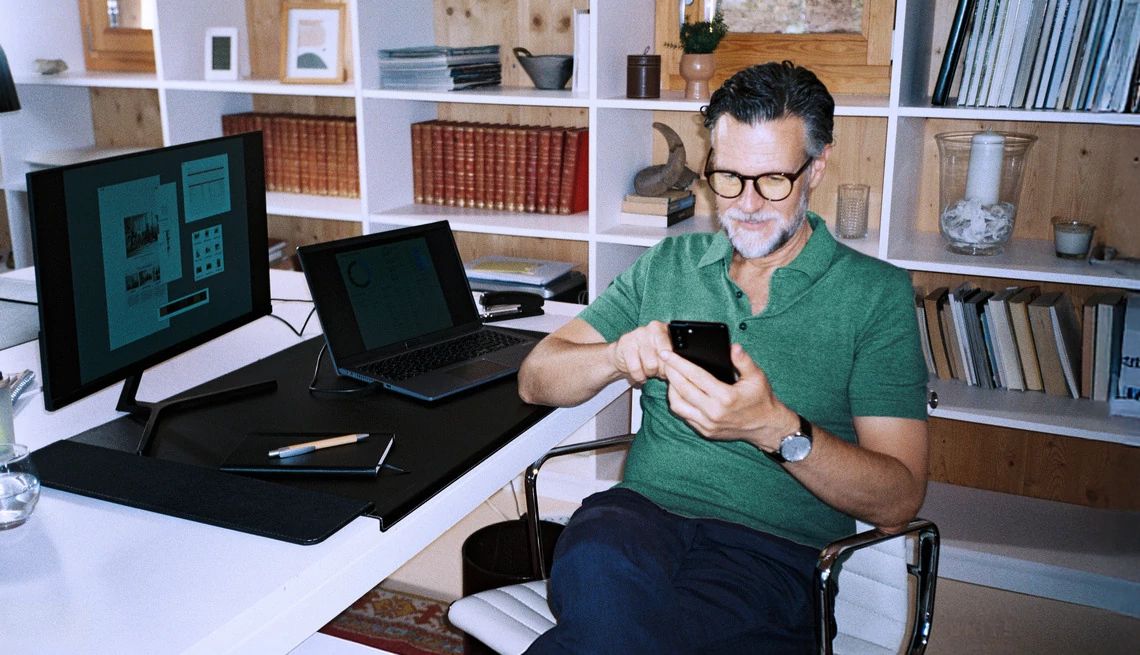 mature white man looking at financial information on computer screen and mobile phone