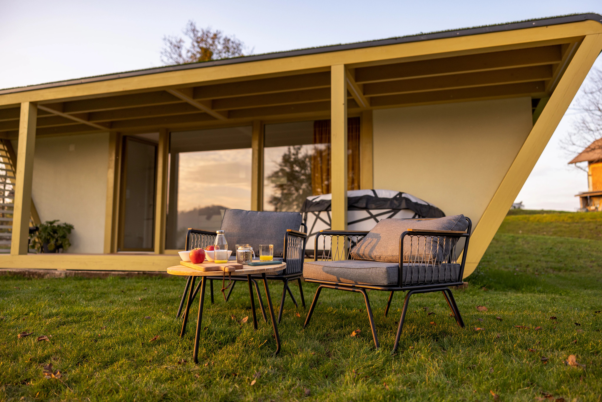 the outside of a single story home with two chairs and a table sitting in the lawn