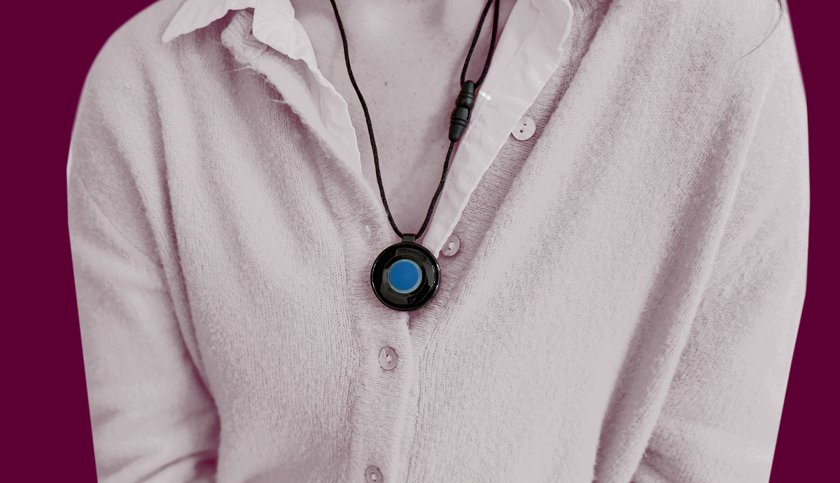 Woman wears a Medical Alert help button around her neck in front of red background