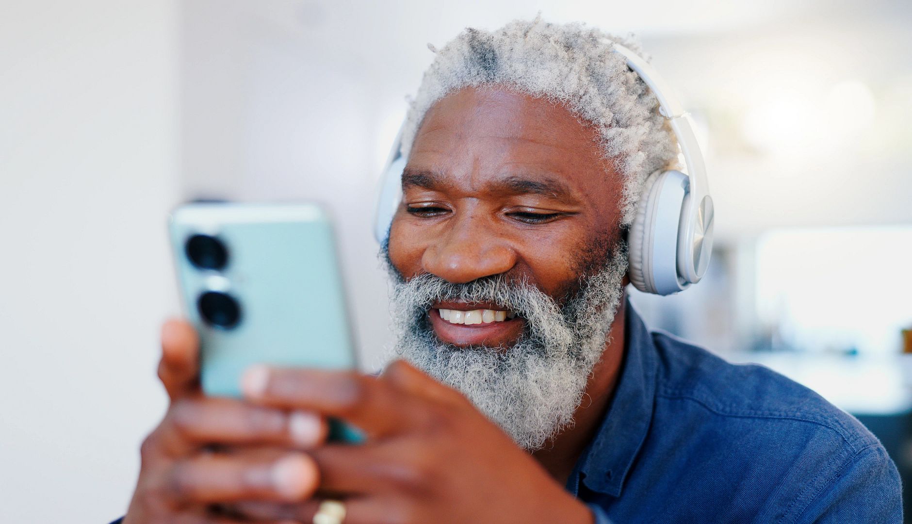 Senior black man, headphones and phone in music or audio streaming, communication or networking at home. Senior black man, headphones and phone in music or audio streaming, communication or networking at home.