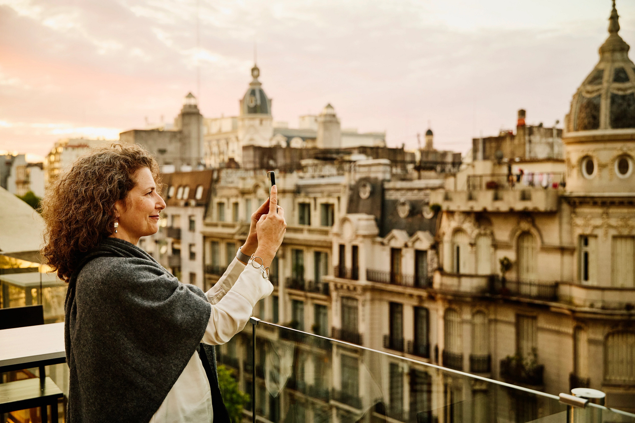 a woman holds a smartphone, taking a photo of buildings