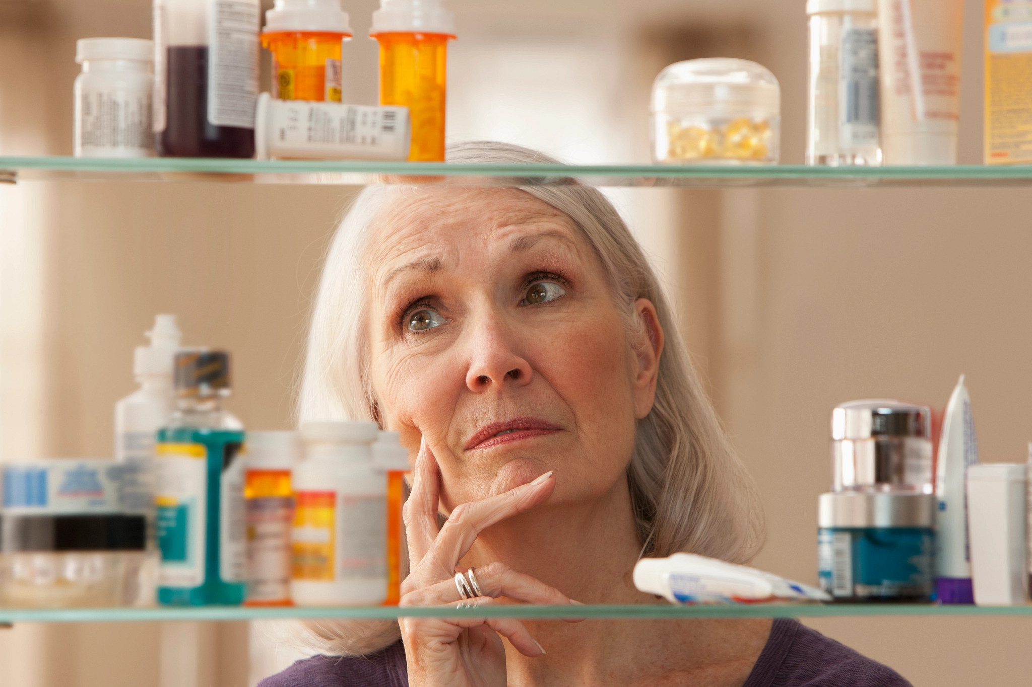 A woman looking thoughtfully into her medicine cabinet