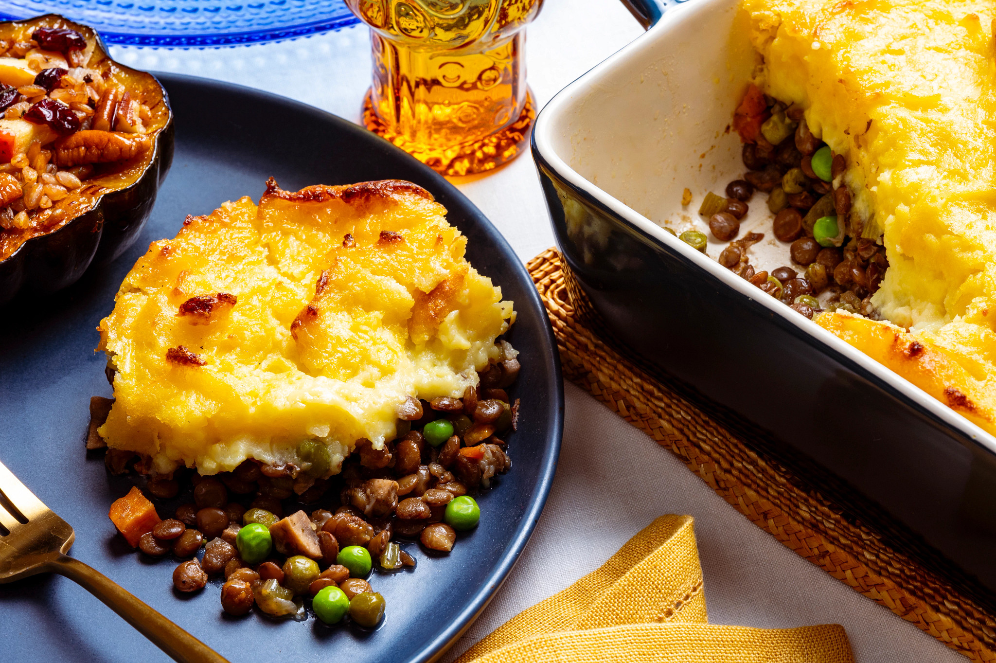 Hearty scoop of lentil shephard's pie on a blue plate with acorn squash on the side.