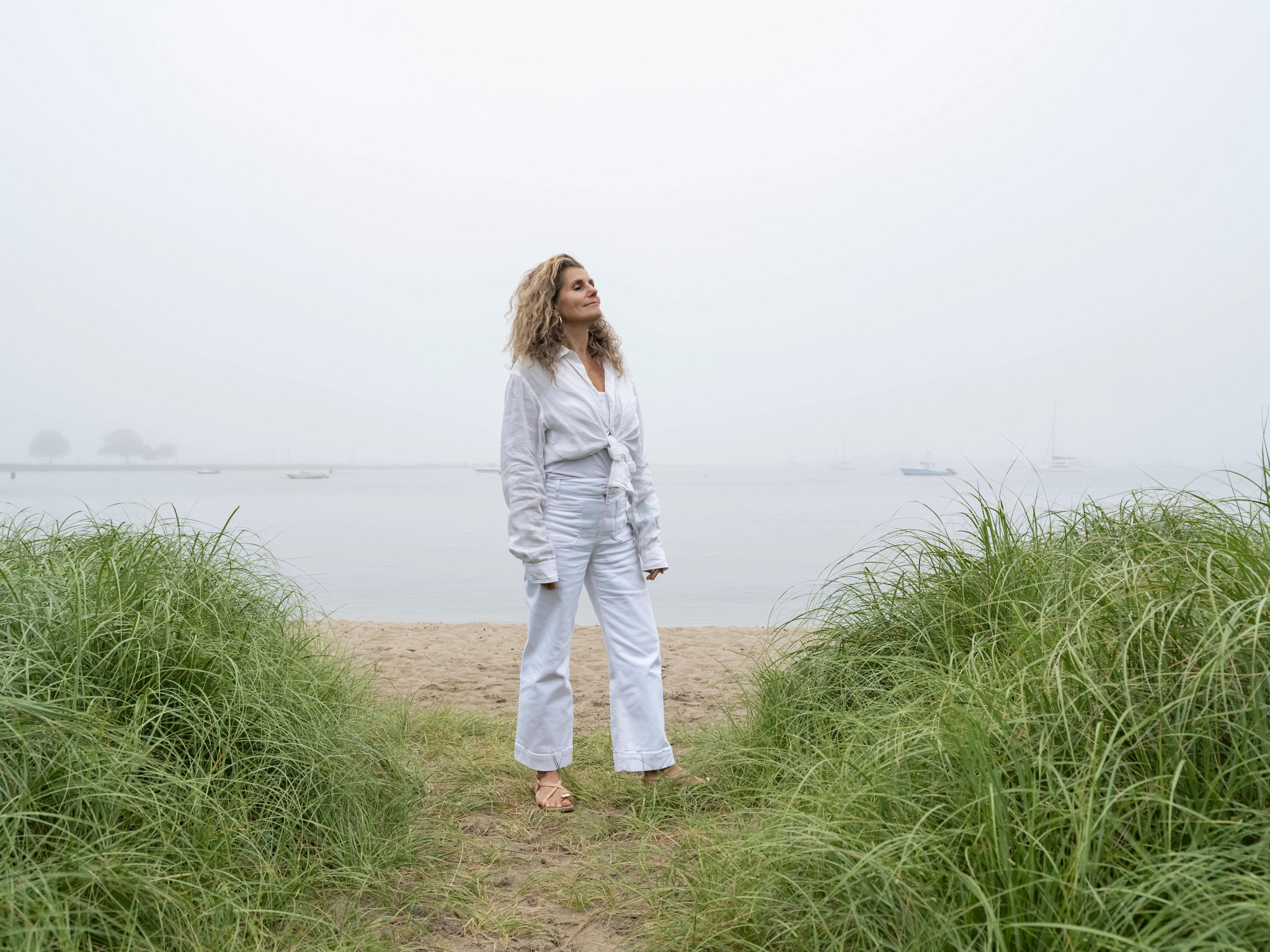 a woman stands on the beach with her eyes closed and face turned up