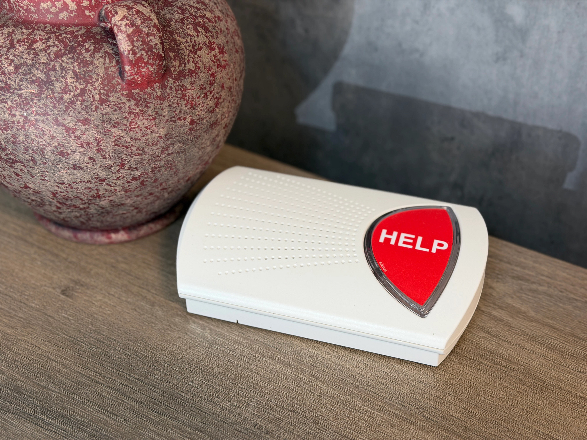 The Bay Alarm Medical SOS Home device on a nightstand next to a vase.