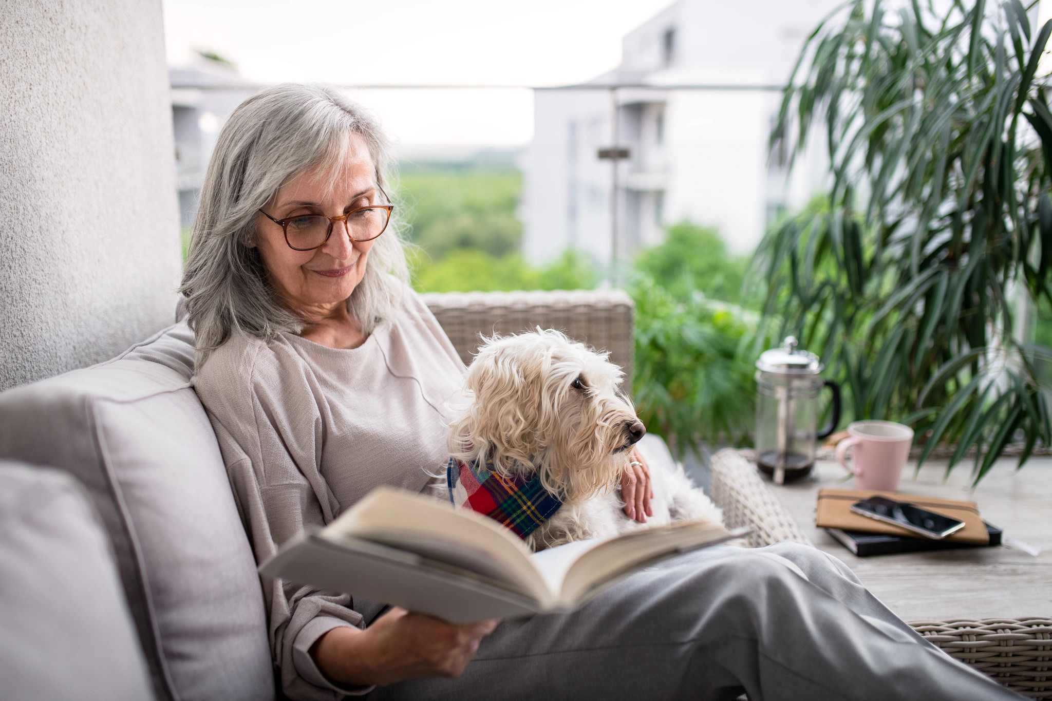 a woman sitting on her couch and reading a hardcover book while holding her dog