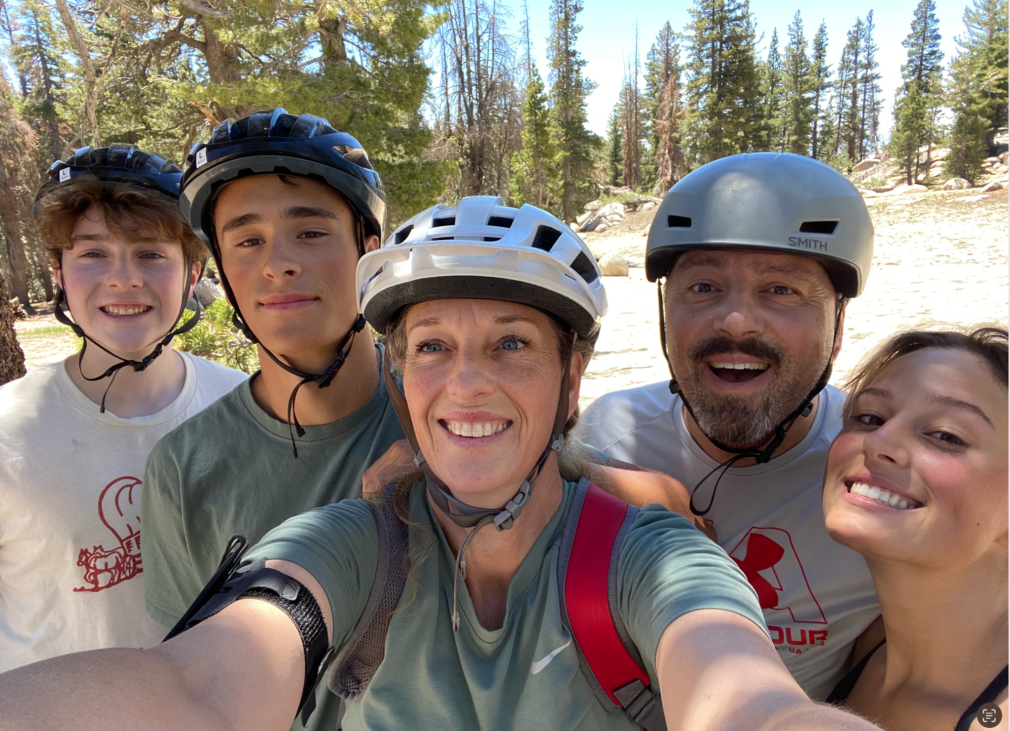 a family posing for a selfie while wearing biking helmets in a wooded area