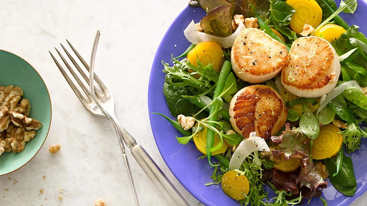 A close-up view of golden beets and green beans with scallops on a plate