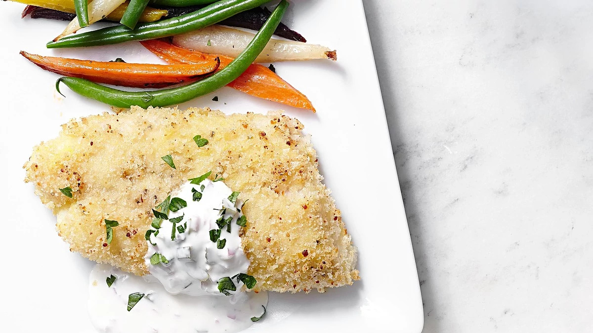 A close-up view of Parmesan-crusted cod with tartar sauce on a plate