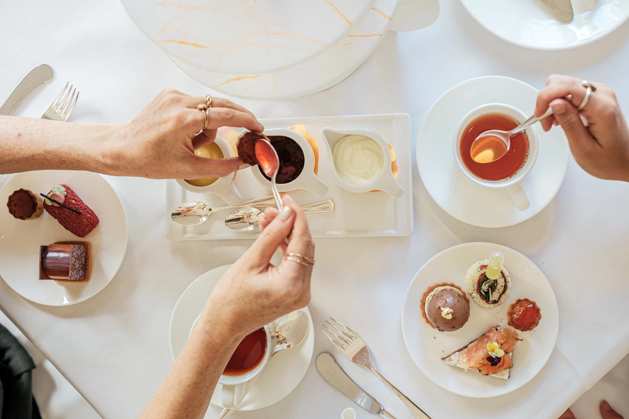 people stirring tea in cups next to desserts
