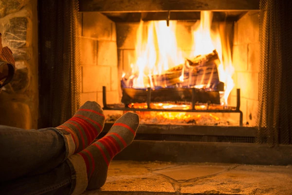 Image of a persons crossed socked feet in front of a lit fireplace.