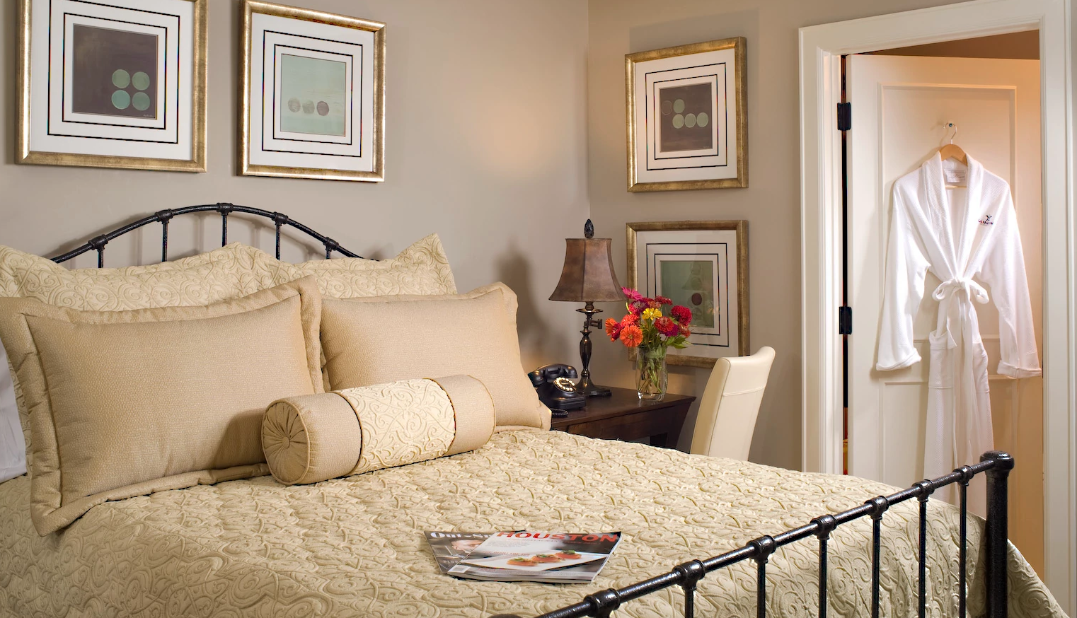 Black-Owned Hotels to Visit a hotel room with cream bedding, art on the walls and a white robe hanging on a door