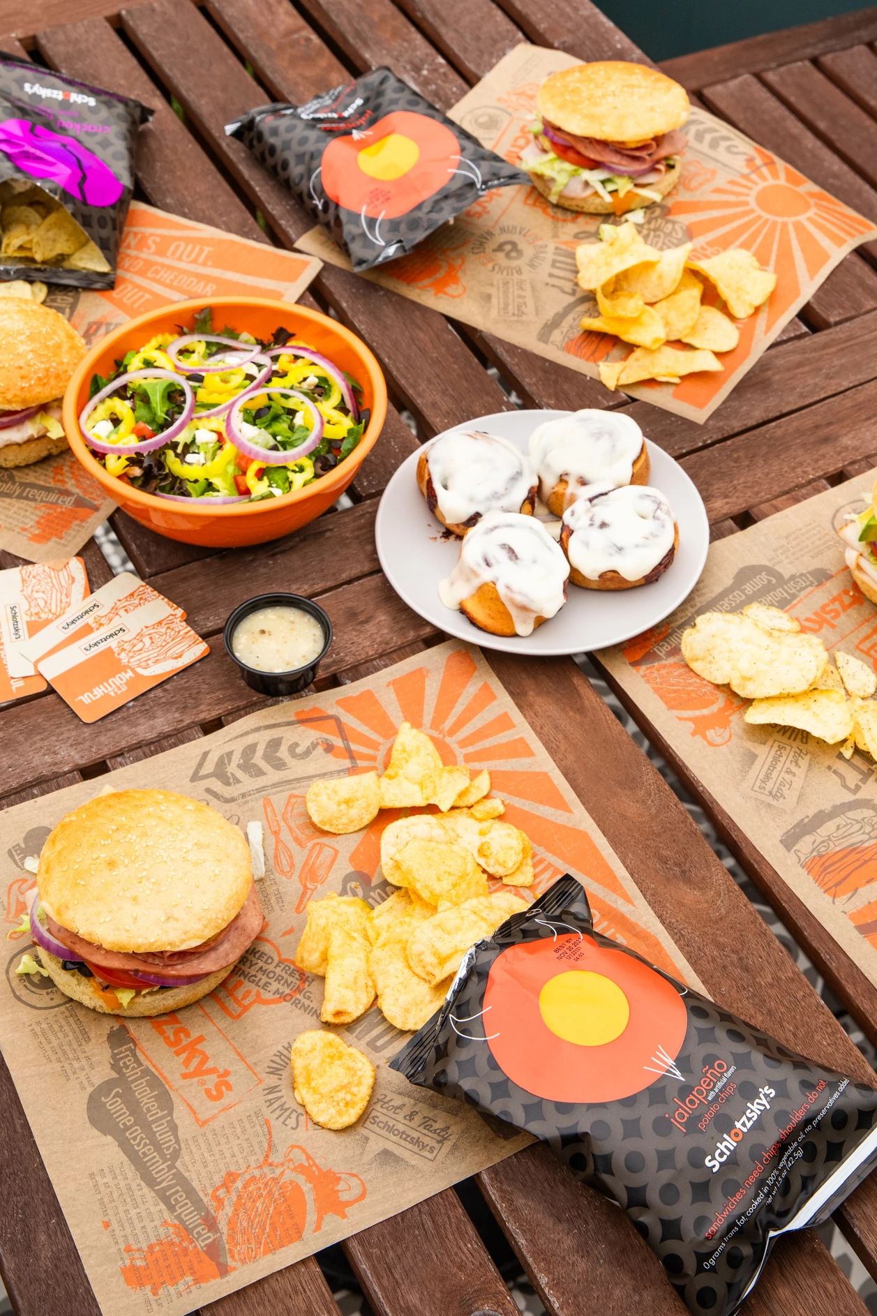 Schlotzsky's sandwiches, chips and dessert on a picnic table