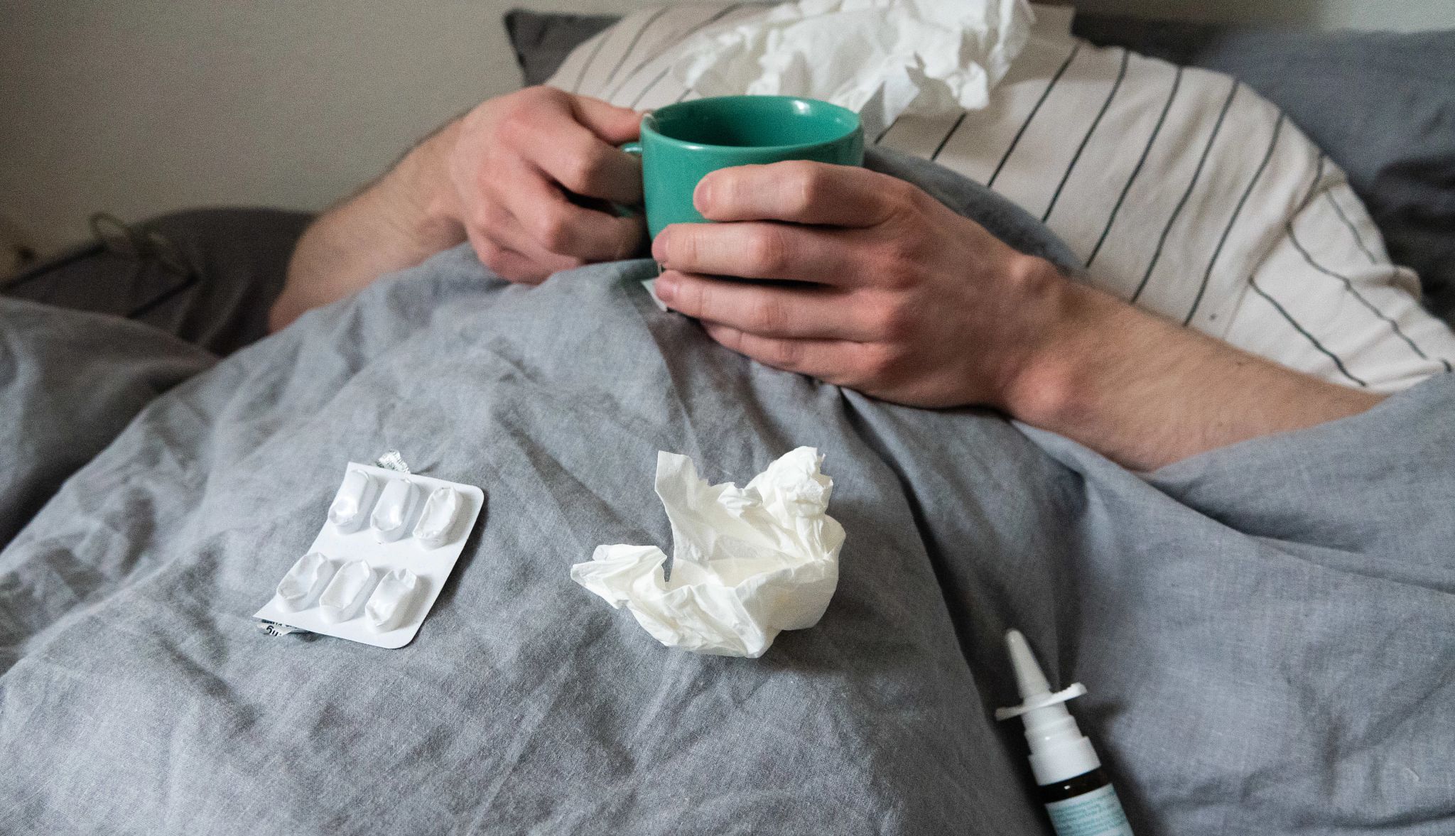 Flu Do's and Don't's man lies in bed with handkerchiefs, teacup, nasal spray and tablets
