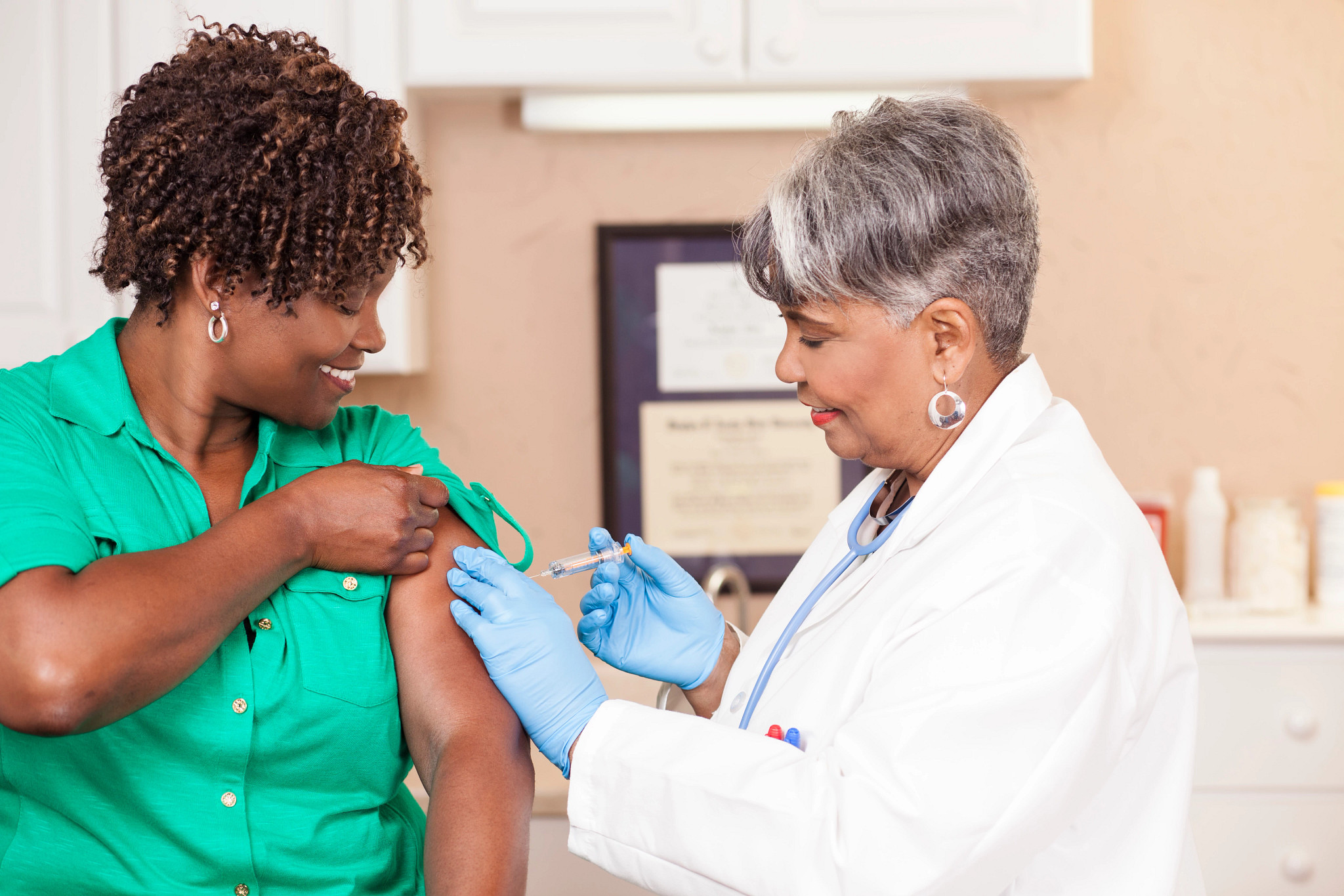 Senior adult doctor or nurse gives flu vaccine to African descent, mid-adult patient at a local medical clinic, hospital, or doctor's office.