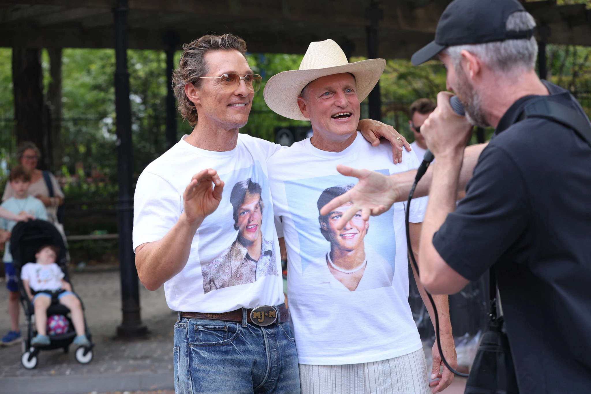 Matthew McConaughey and Woody Harreslon with their arms over one anothers shoulders while talking to a third person