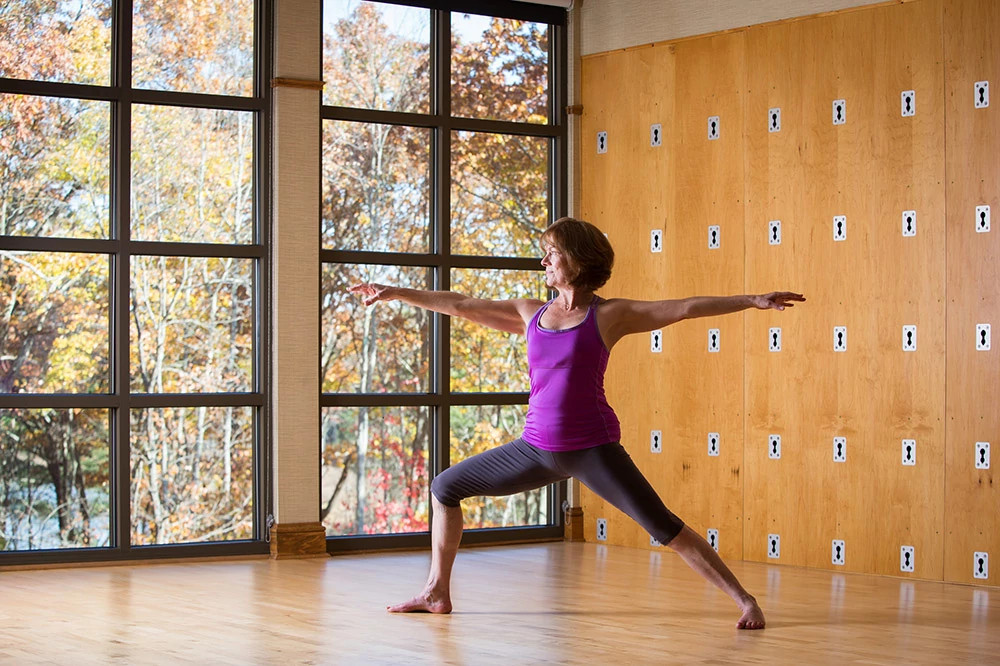 Person practicing a yoga warrior pose in a spa studio overlooking an autumn forest