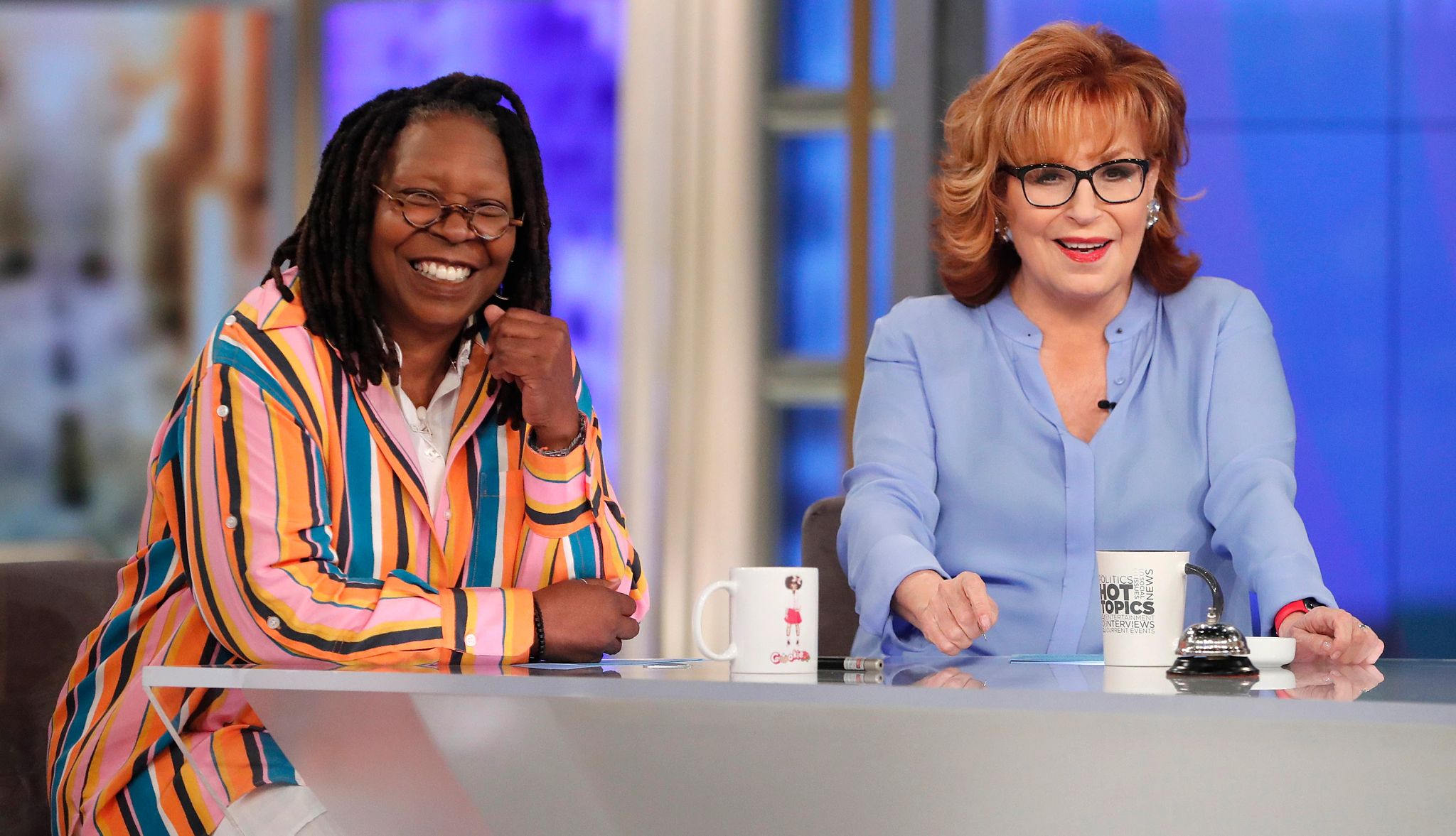 Whoopi Goldberg and Joy Behar on 'The View' Whoopi Goldberg sitting next to Joy Behar at a desk with a mug in front of each of them