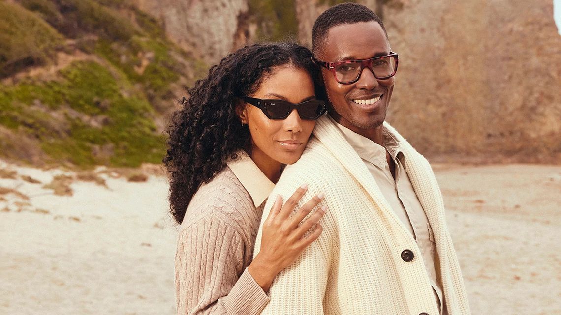 A couple smiling on the beach wearing stylish sunglasses from LensCrafters