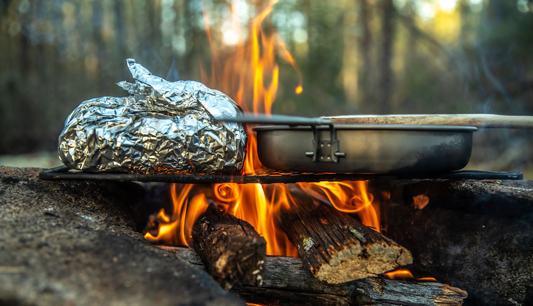 Campfire Food food wrapped in tin foil next to a pan on a grill