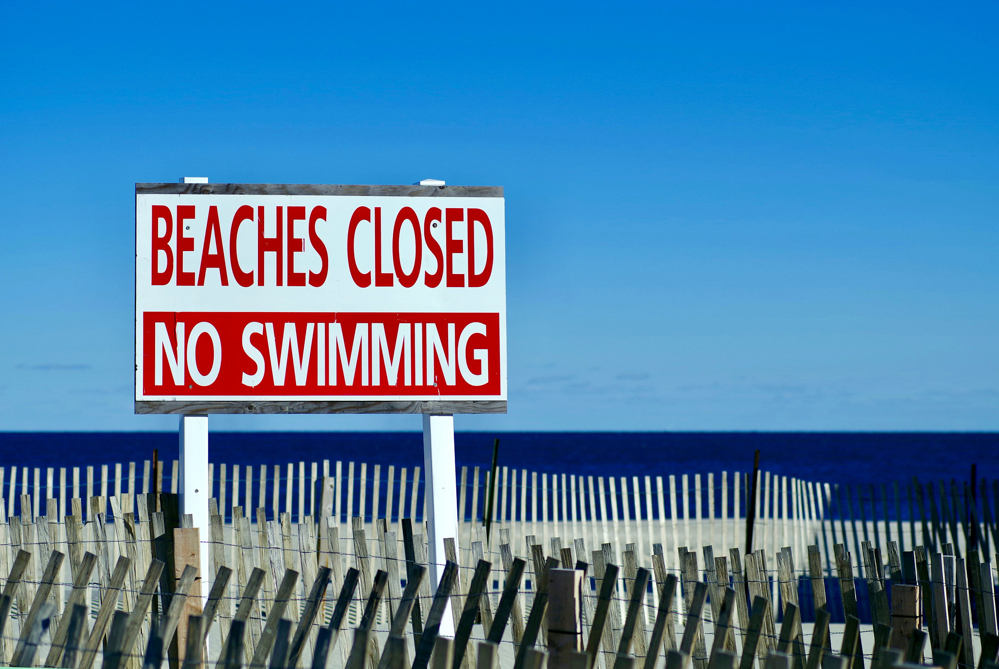 two blue umbrellas erected on a beach next to a beach closure sign