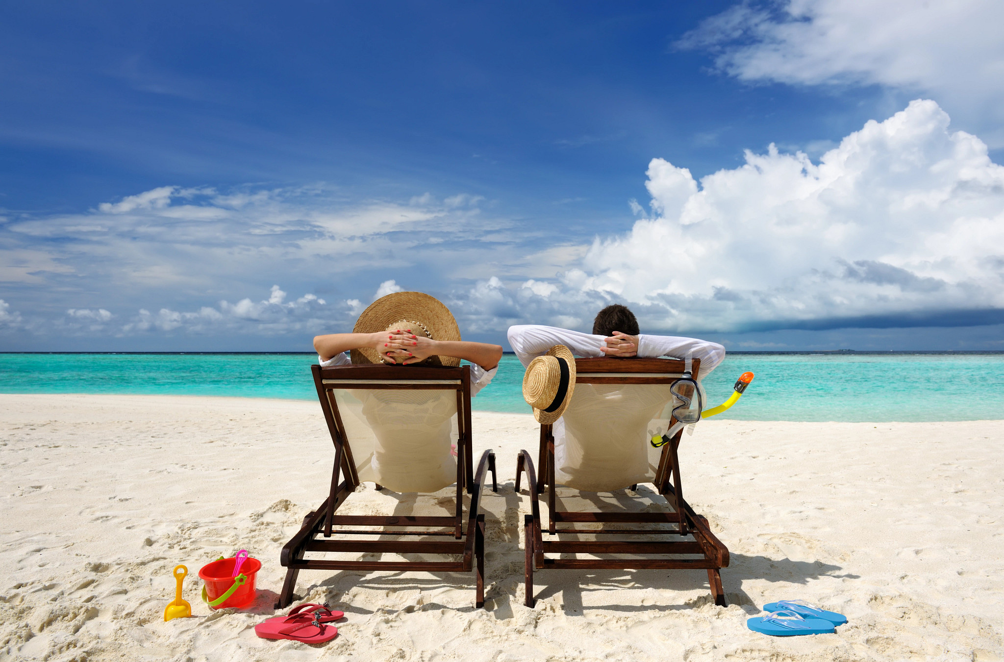 Two AARP members relaxing on a tropical beach in recliner chairs while on vacation that they planned with AARP travel benefits