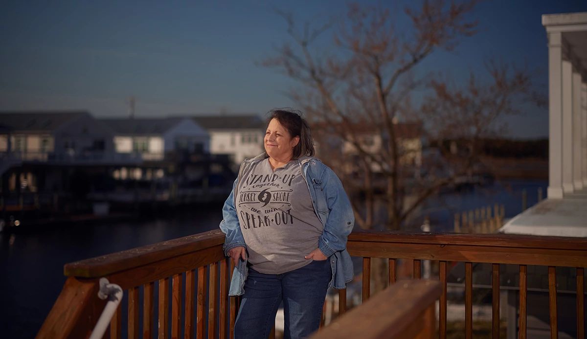A woman in a gray sweatshirt and blue jeans stands on her deck