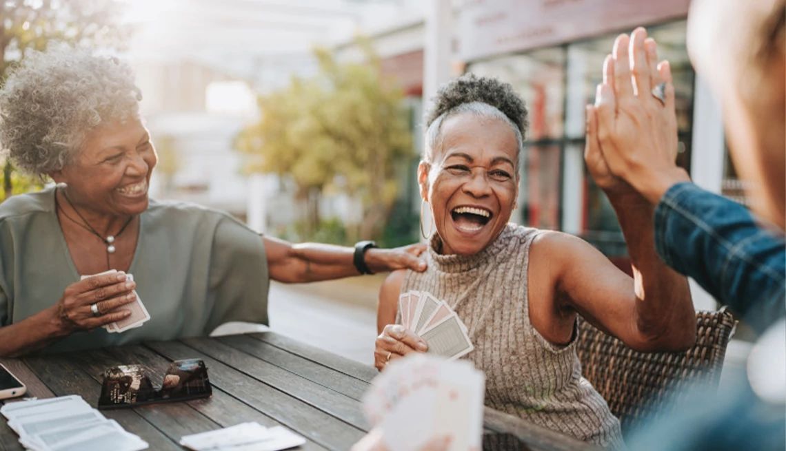 Women playing cards and laughing on patio table outdoors