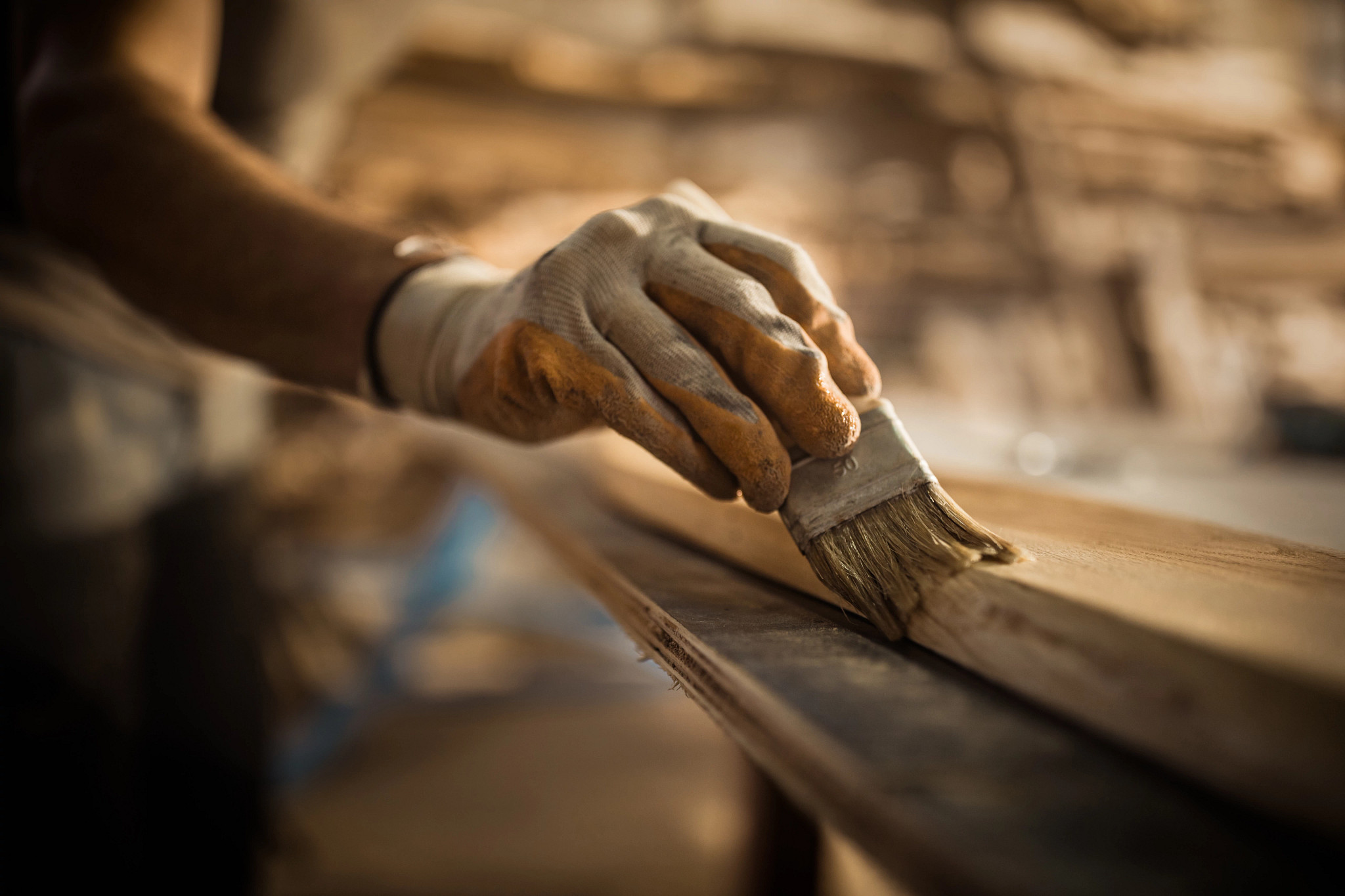 Close up of carpenter using brush while applying protective varnish to a piece of wood.
