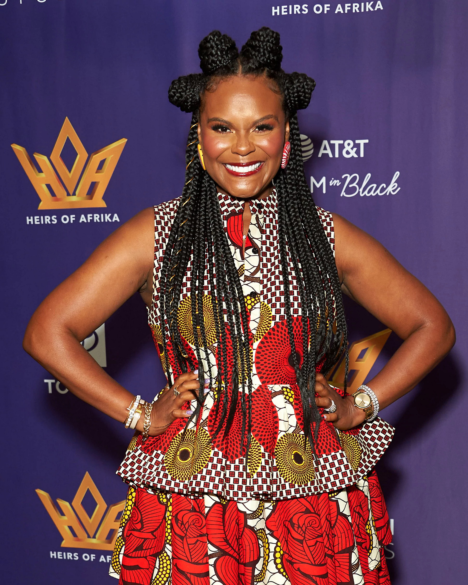 Tabitha Brown posing at an event in a colorful patterned outfit with an elaborate braided hairstyle