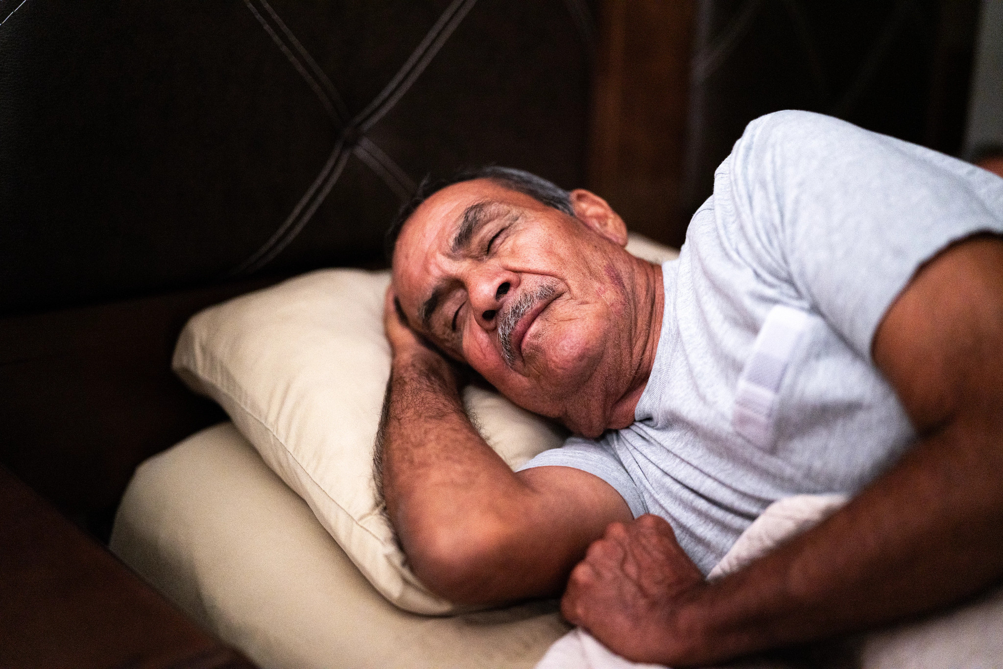 A man sleeping in a bed with his head on his hand on the pillow