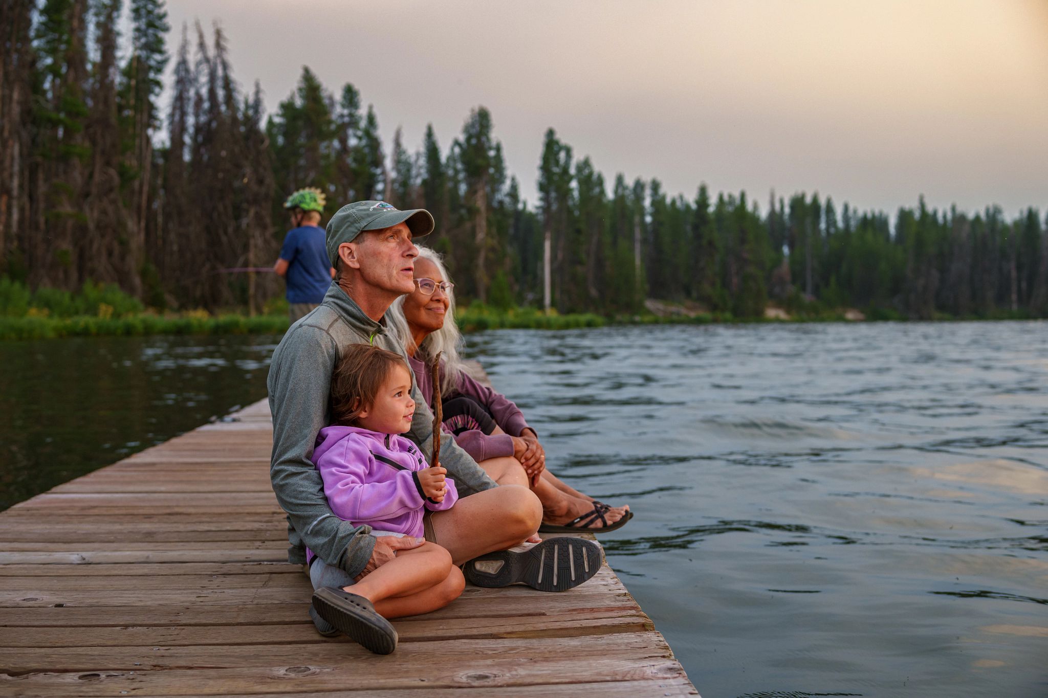 Parents sitting with their daughter by a lake.