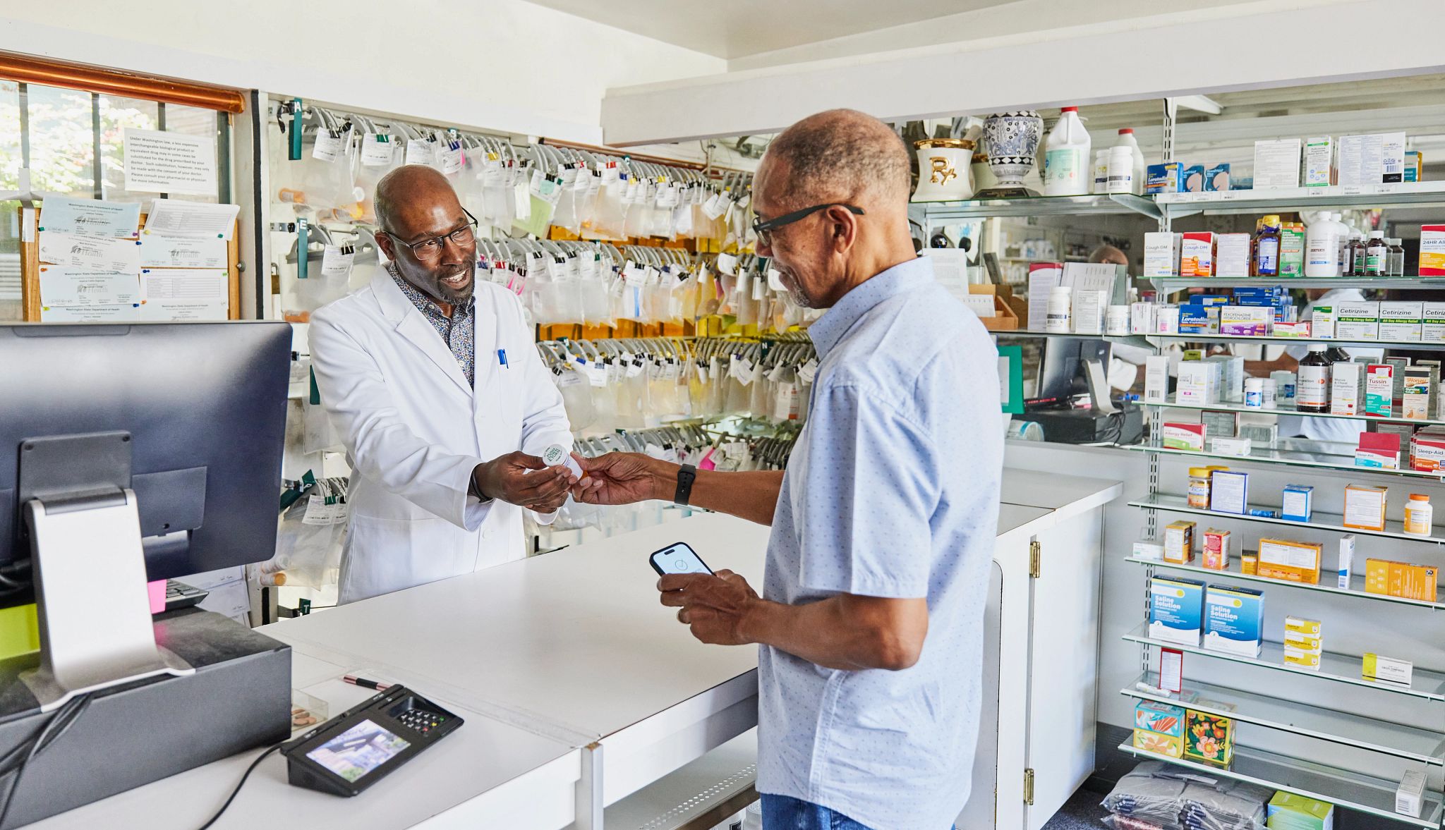 Medium shot of smiling pharmacist handing prescription to senior patient at counter in pharmacy