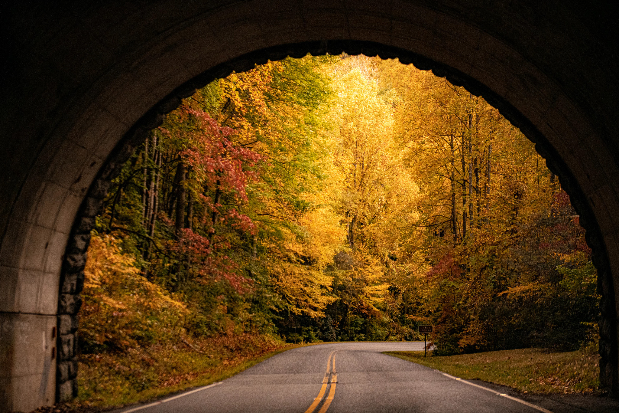 Quiet roadway passing beneath a stone bridge surrounded by golden autumn trees and colorful fall foliage
