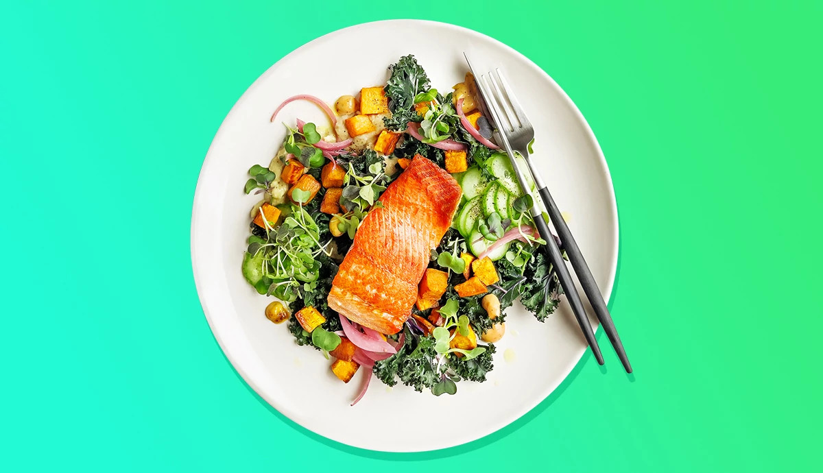 Seared salmon fillet topped over a kale and vegetable salad on a white plate.