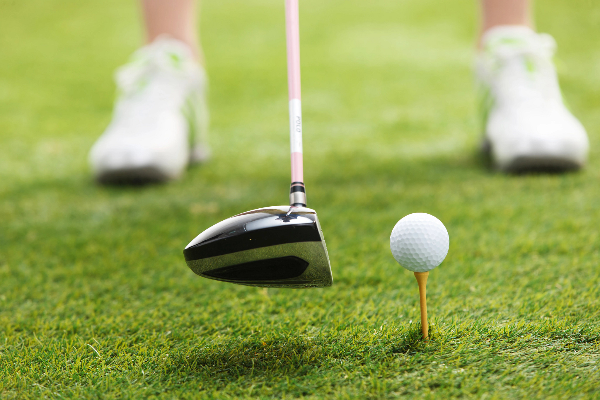 A close-up of a golf club about to hit a white ball on a yellow tee in the grass.