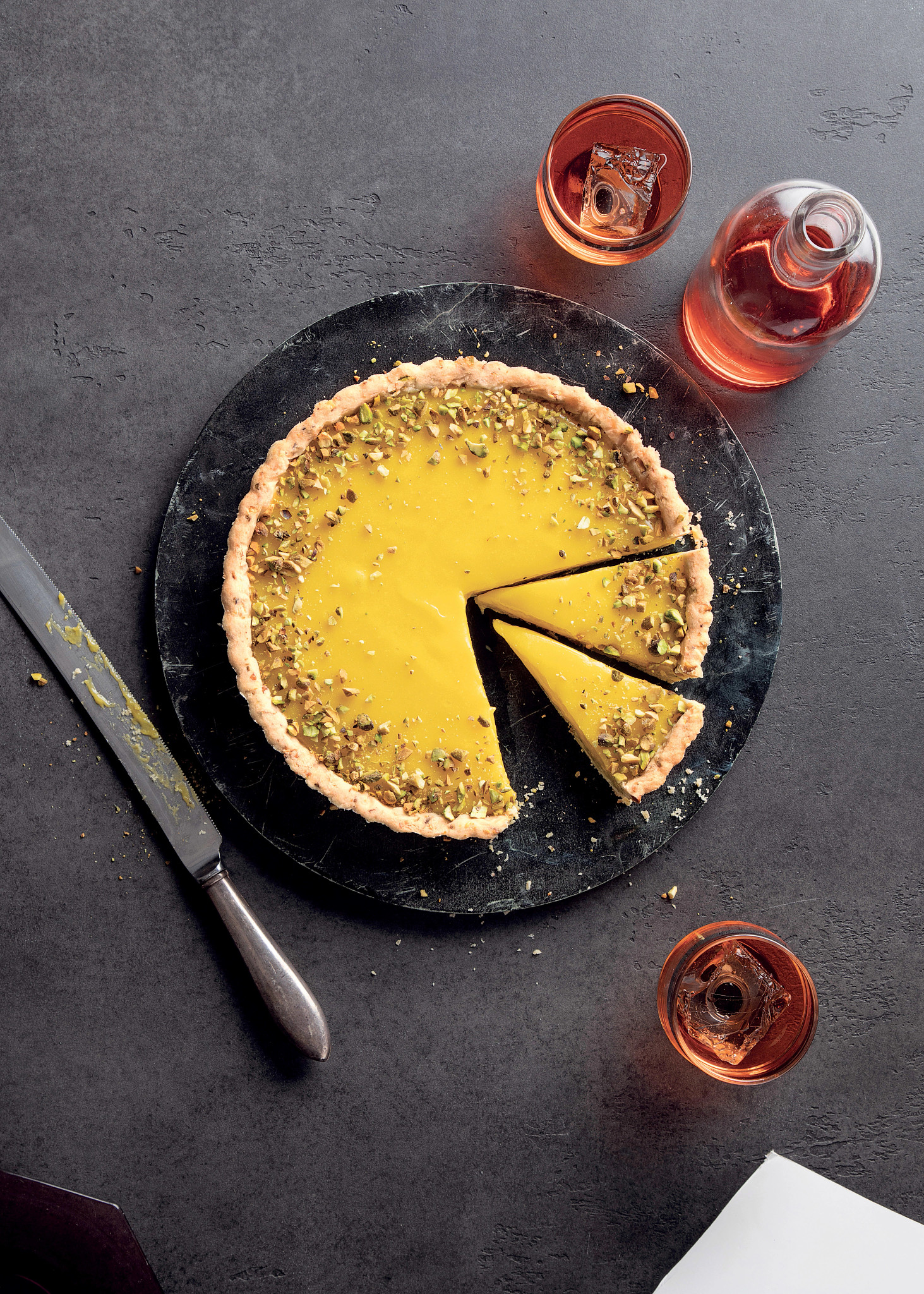 Limoncello Pistachio Tart with a couple slices cut on a dish with knife and drinking glasses next to it