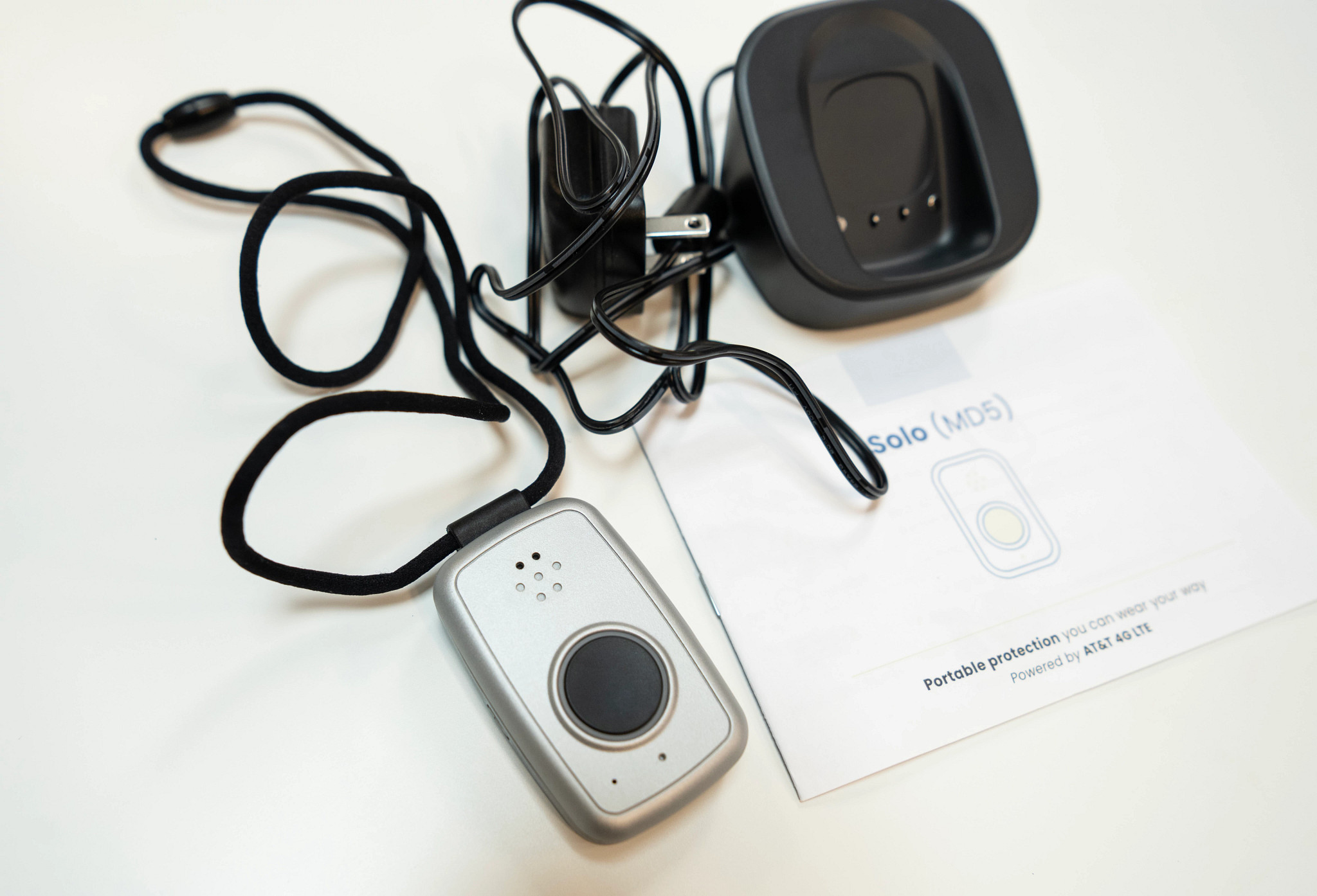The MobileHelp Solo pendant next to the manual and charger on a white table.