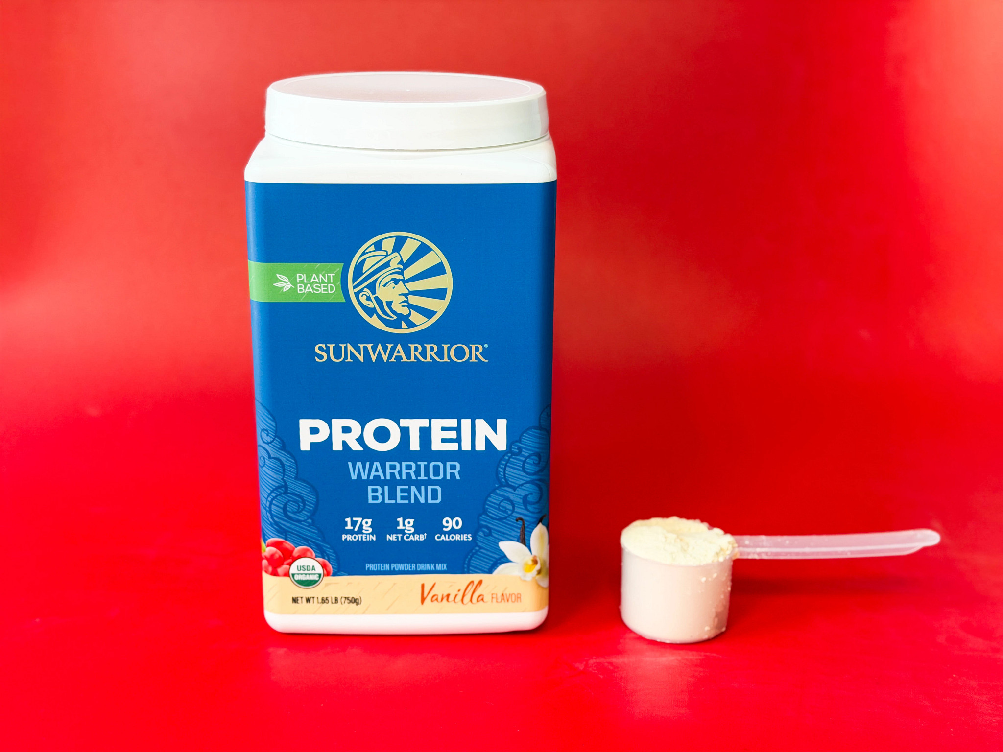 A container and scooper of Sunwarrior Protein Warrior Blend powder on a red background