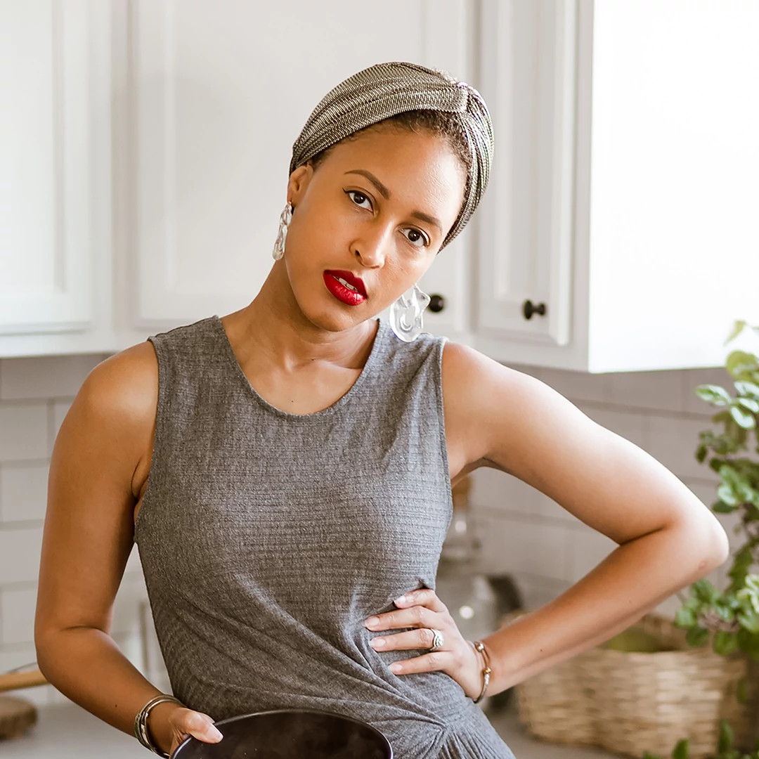 A person standing in a bright kitchen wears a sleeveless dress and headband while holding a bowl