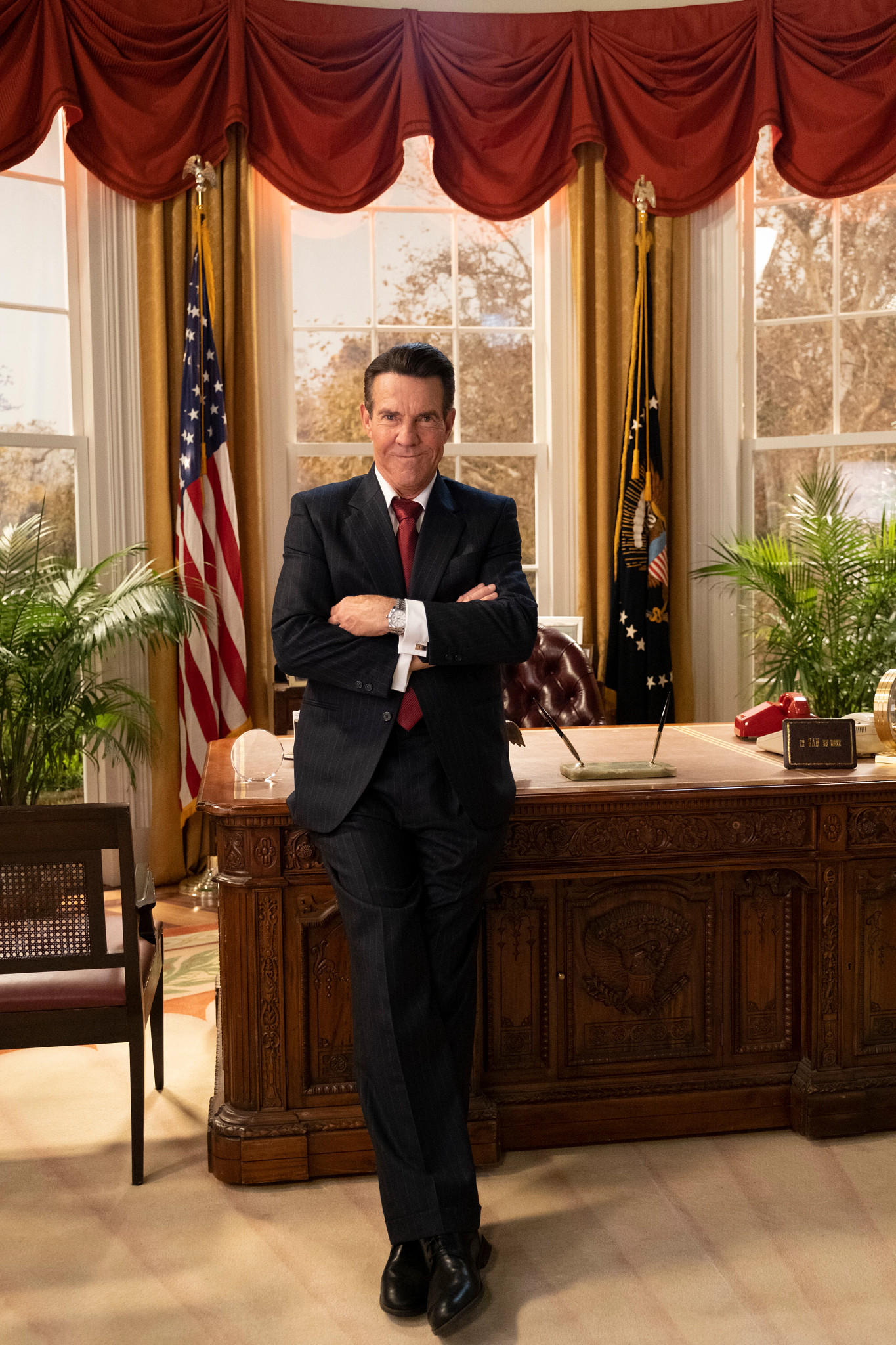 Dennis Quaid as Ronald Reagan in front of desk in what looks like the oval office in a still from Reagan