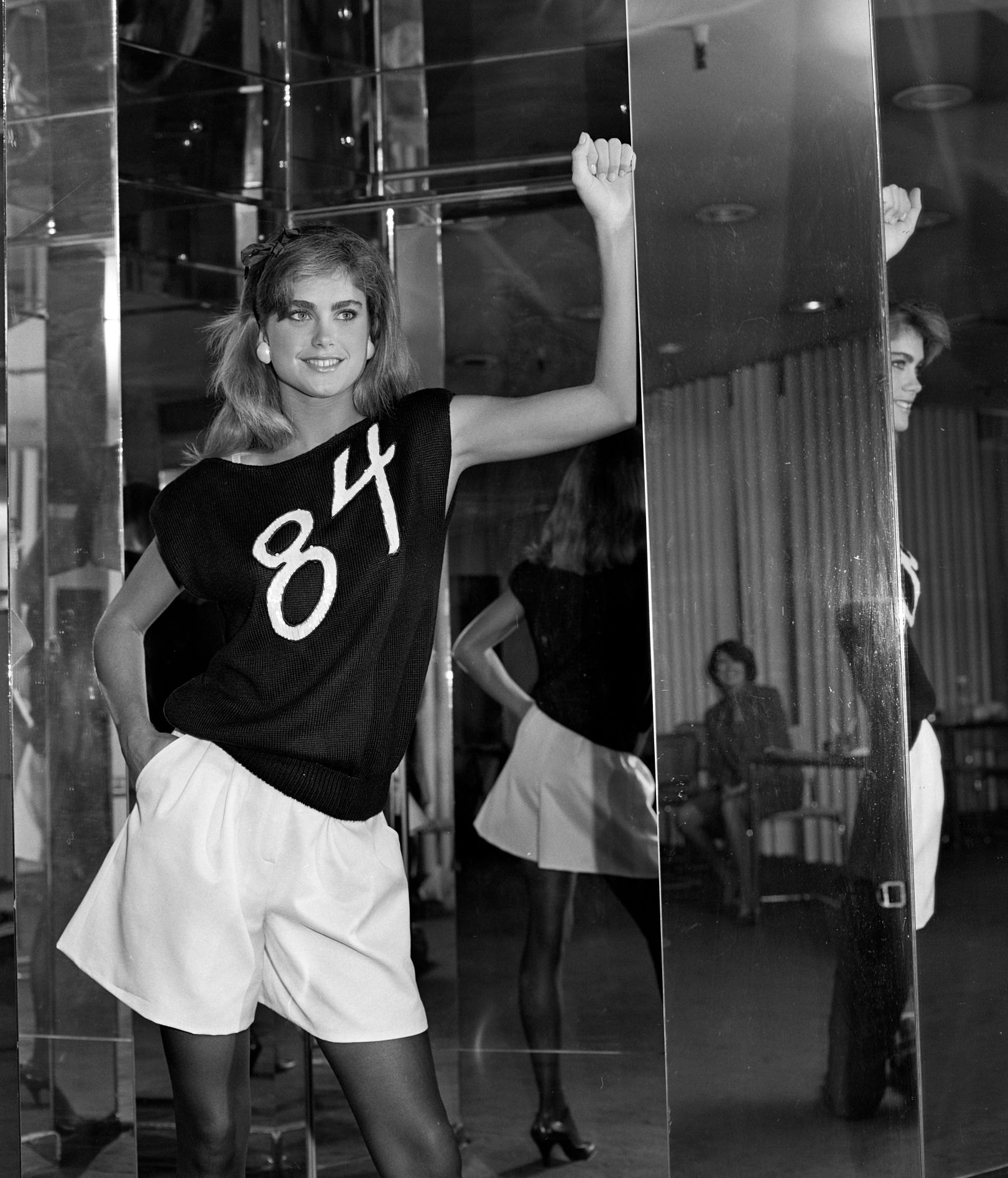Kathy Ireland with full-length mirrors all around her, wearing black shirt with number 84 on it and white shorts